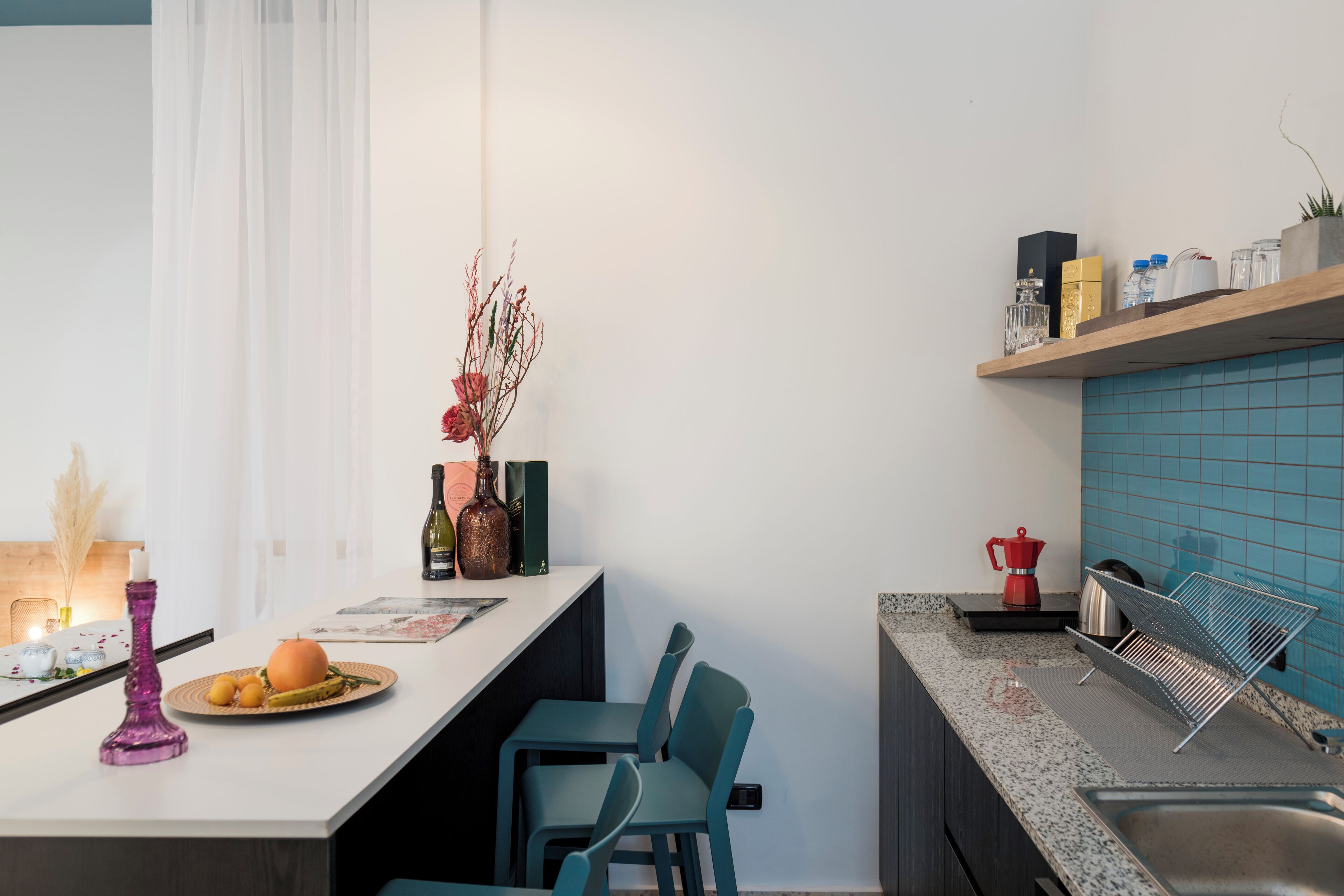 A modern kitchen with a white countertop, teal chairs, and a blue backsplash.