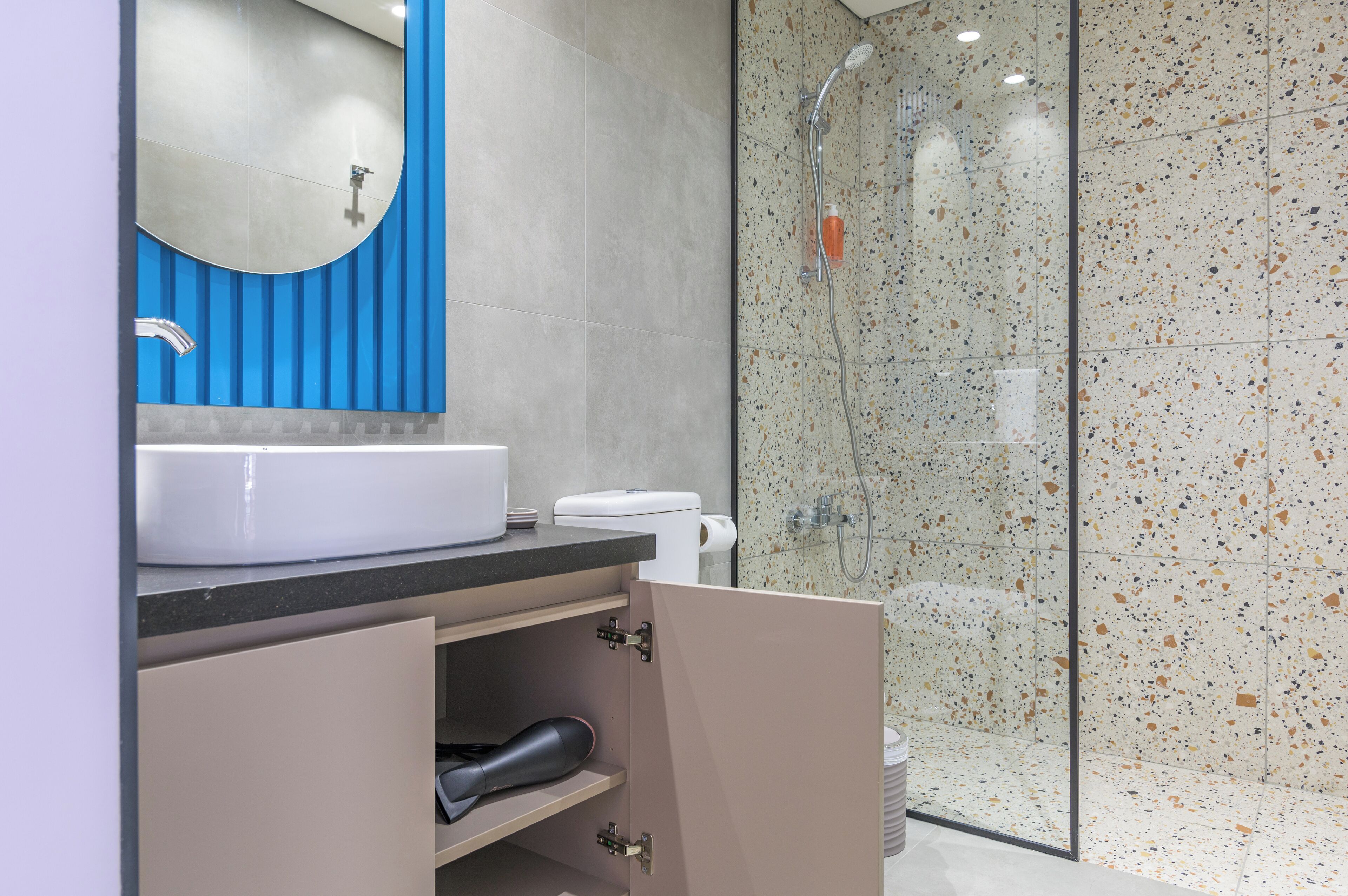 A modern bathroom with a white sink, blue vanity, and a glass shower enclosure.