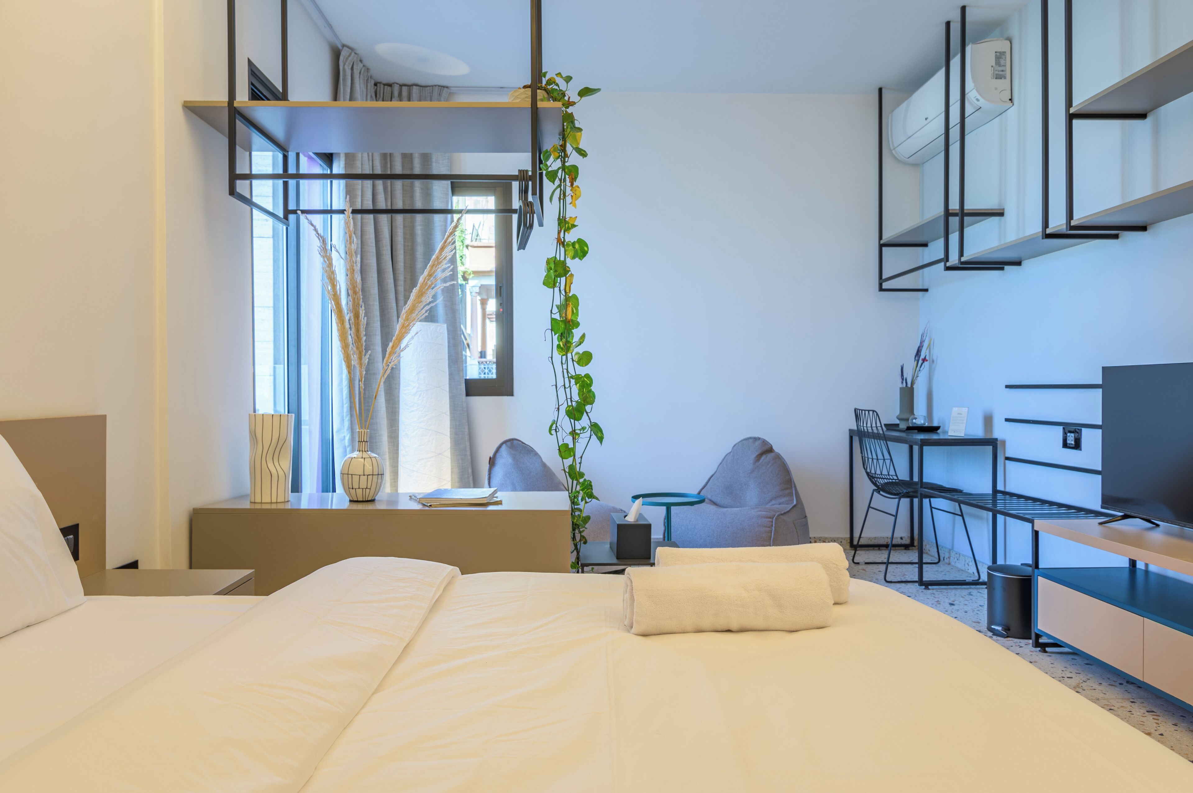 A modern hotel room with a large bed, a desk with a chair, a TV, and a small table with a plant.