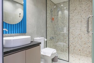 A modern bathroom with a large white sink, a toilet, and a glass-enclosed shower area.