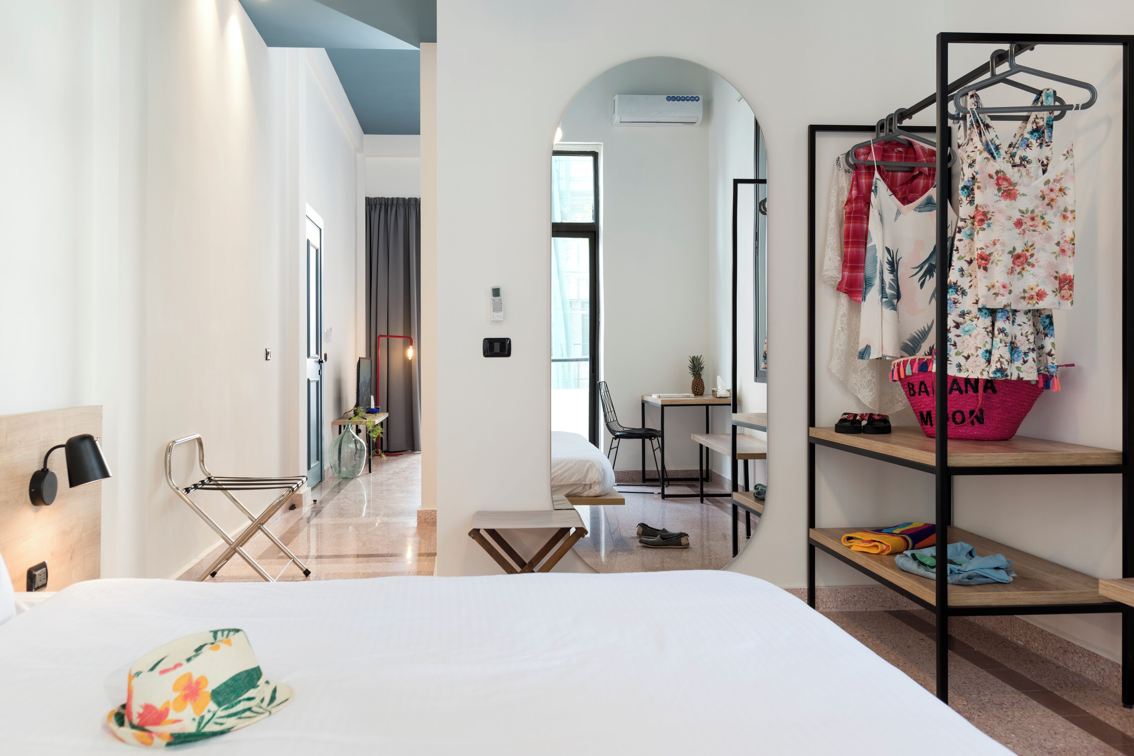 A hotel room with a bed, a chair, a desk, and a clothing rack.
