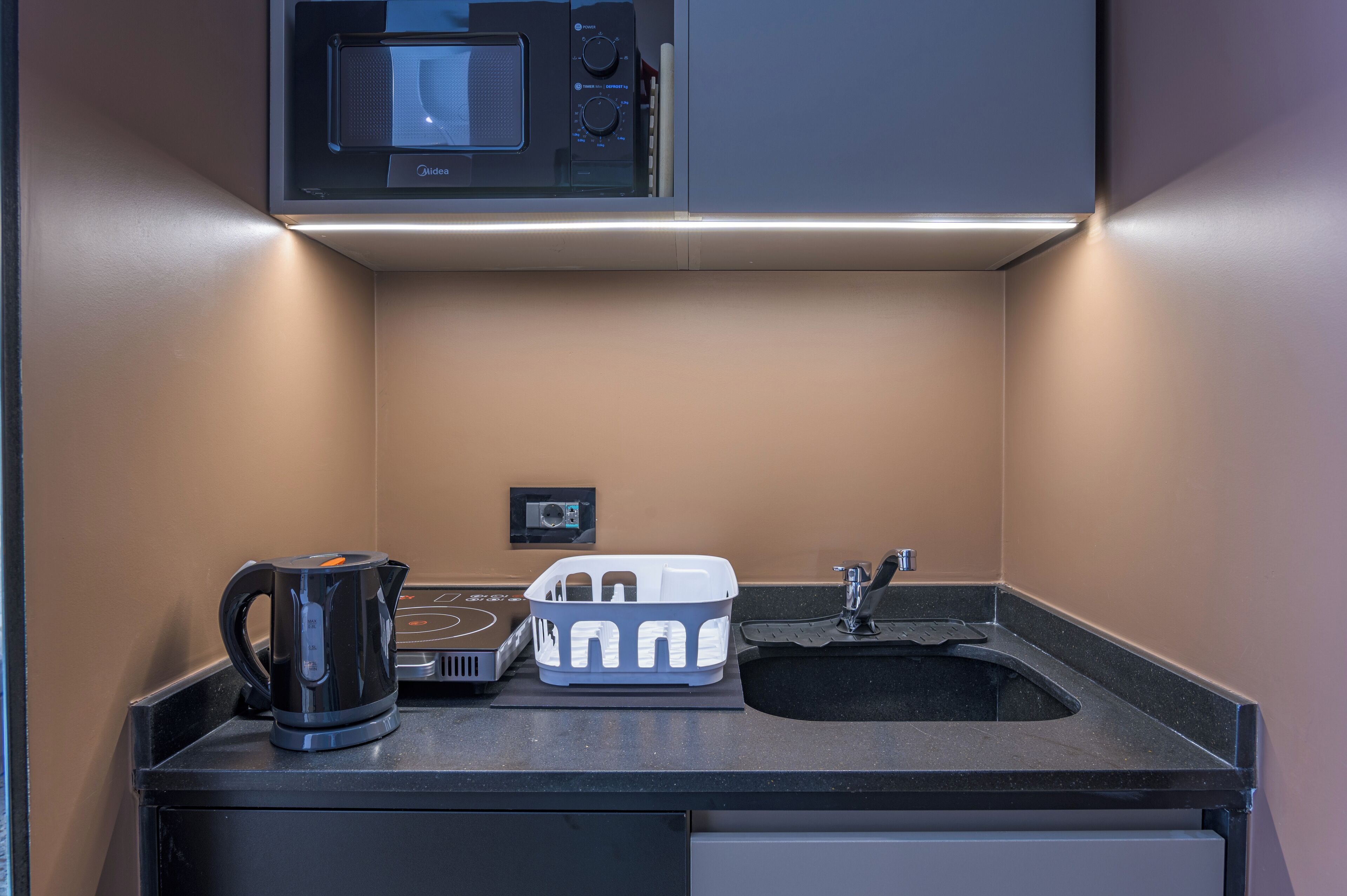 Een kleine keuken met een magnetron, waterkoker en een klein spoelbakje.