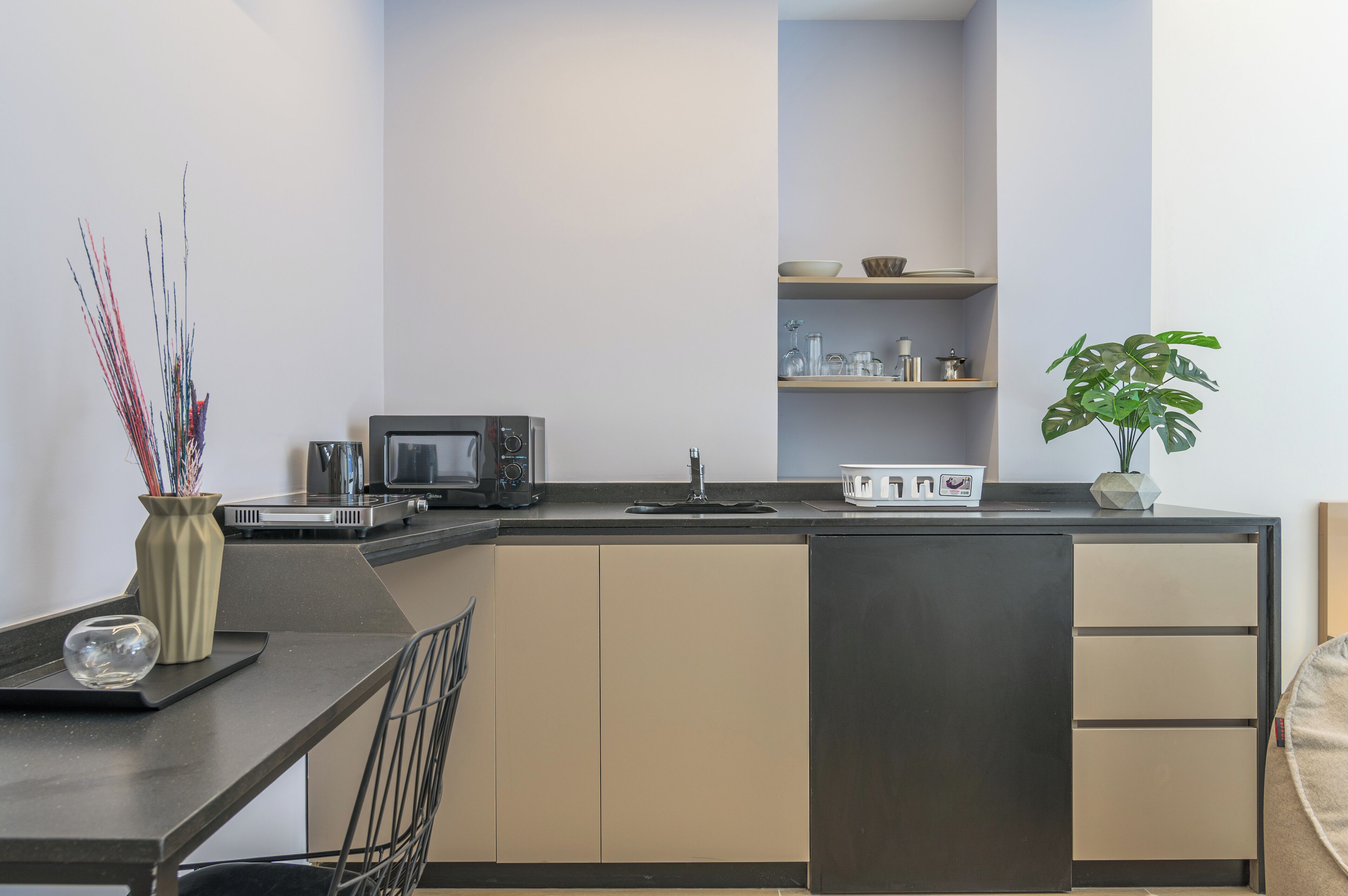 A modern kitchen with a dark countertop, a microwave, and a sink. There is a plant on the counter and a vase with decorative branches.