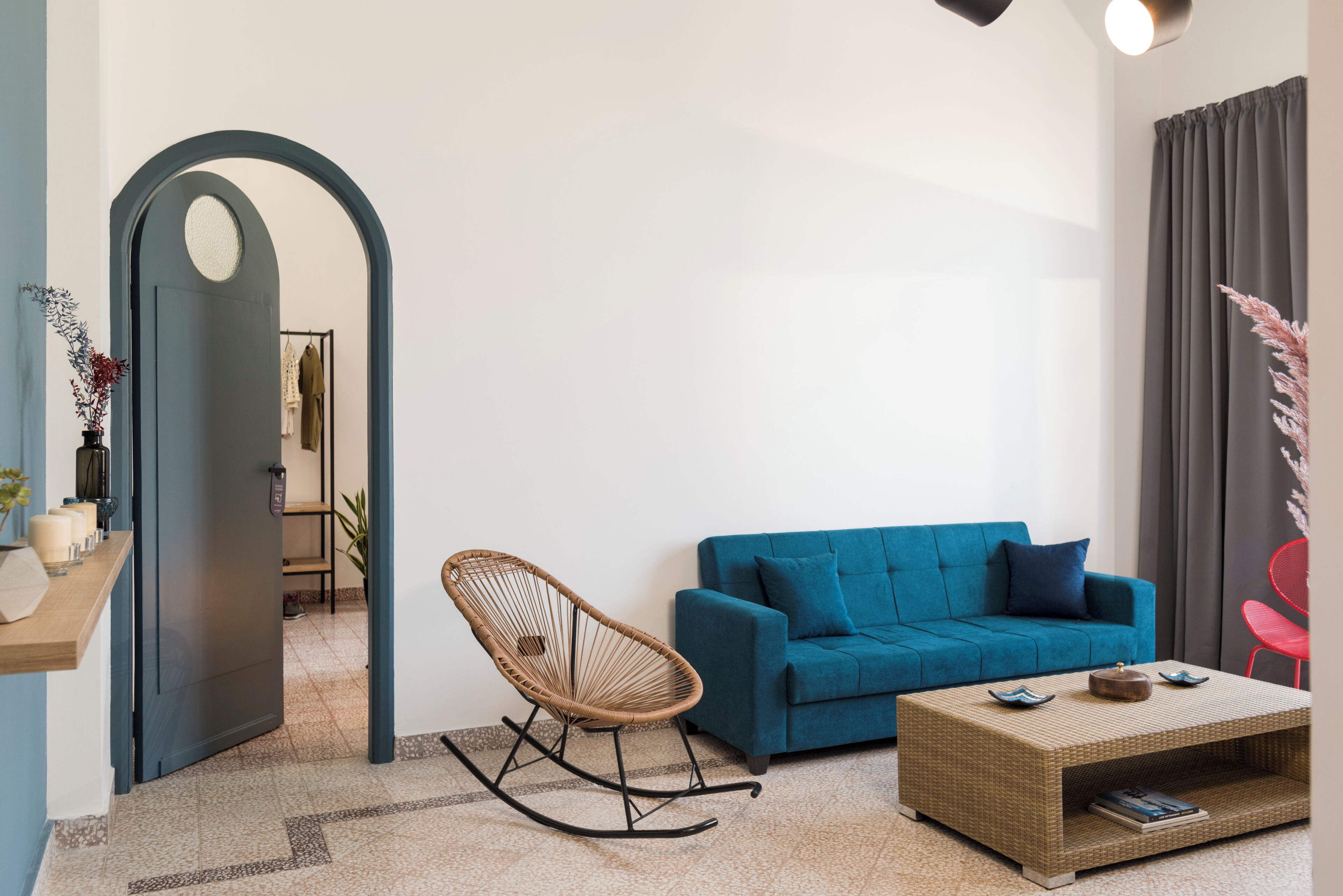 A modern living room with a blue sofa, a rocking chair, a coffee table, and a doorway leading to another room.