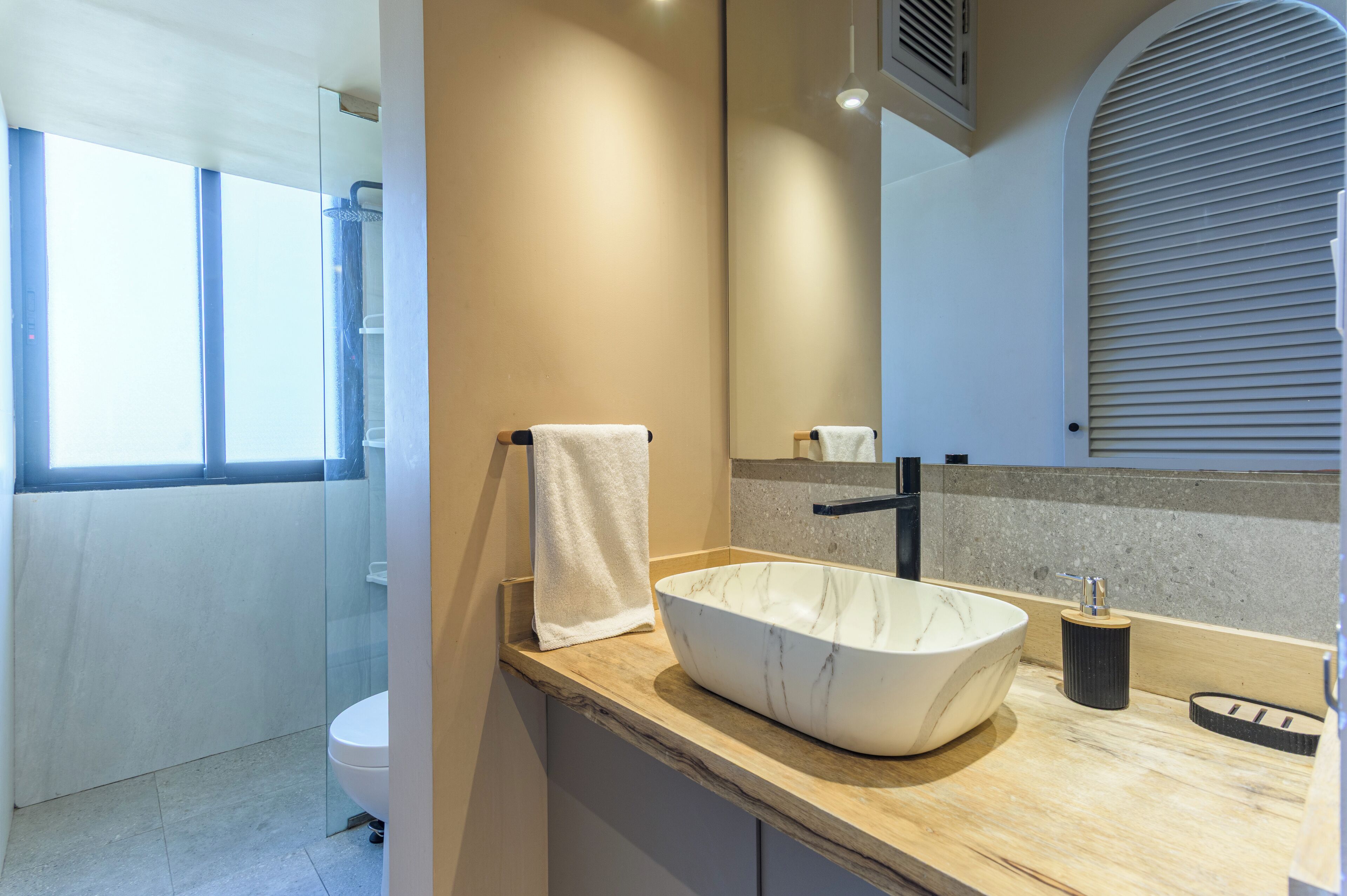A modern bathroom with a large mirror, a white marble sink, and a glass shower enclosure.