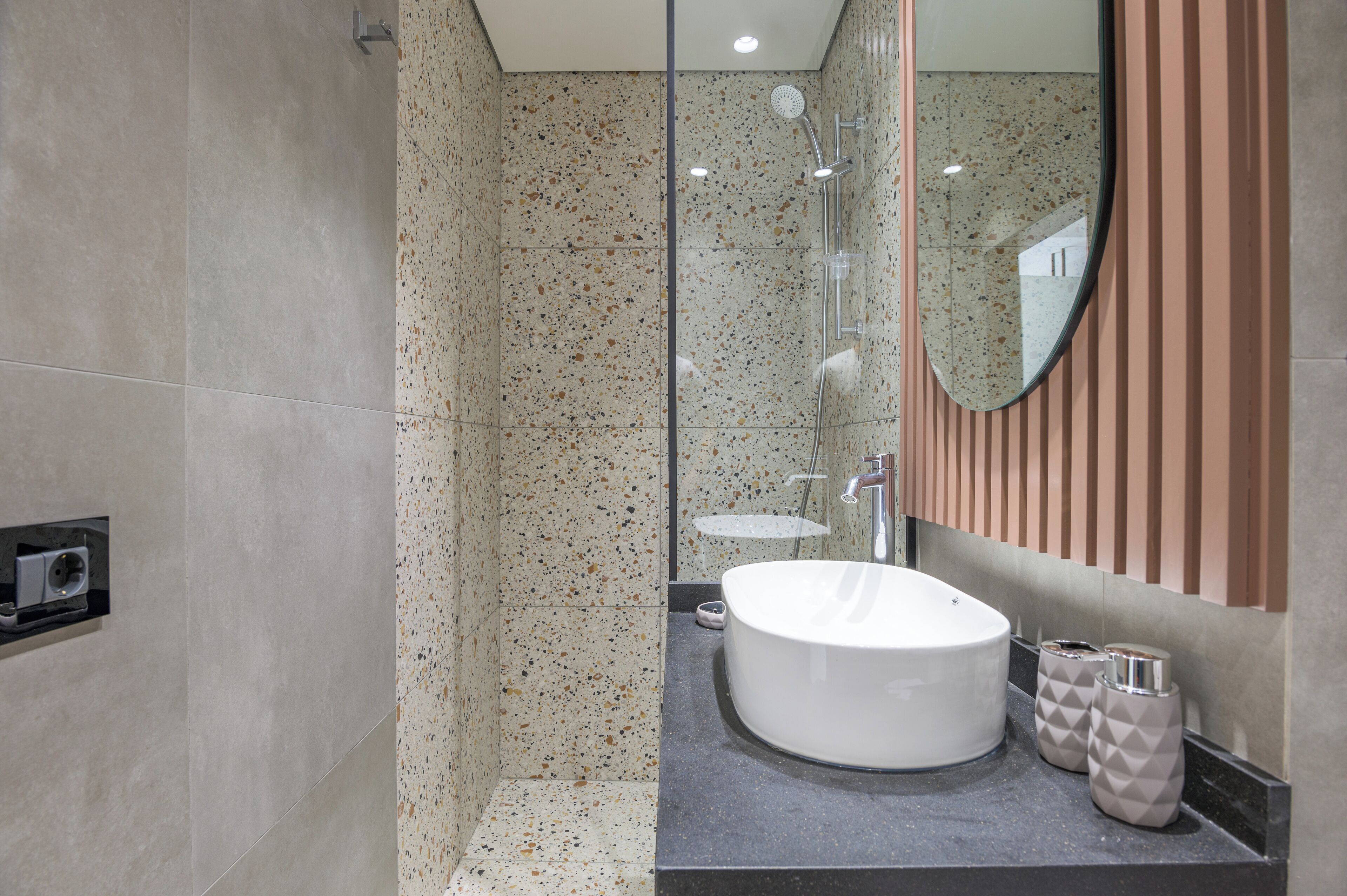 Un baño moderno con un lavamanos independiente, una cabina de ducha de vidrio y un espejo con diseño de panel de madera.