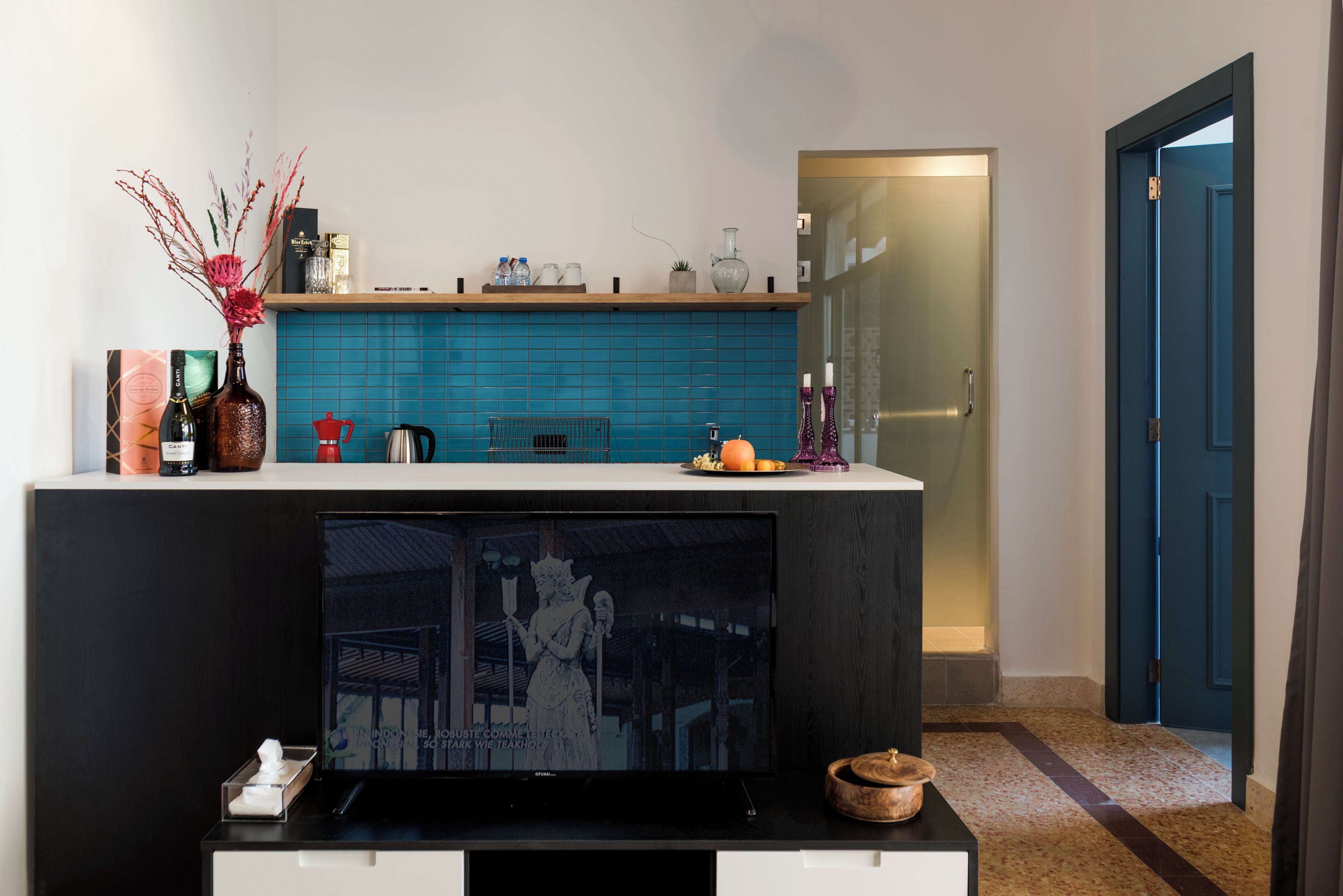 Een moderne keuken met een blauwe tegelwand, een flatscreen televisie en diverse keukenbenodigdheden op het aanrecht.