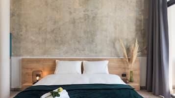 Una habitación de hotel moderna con una cama grande, cabecera de madera, mesita de noche con lámpara y un florero con plantas secas.
