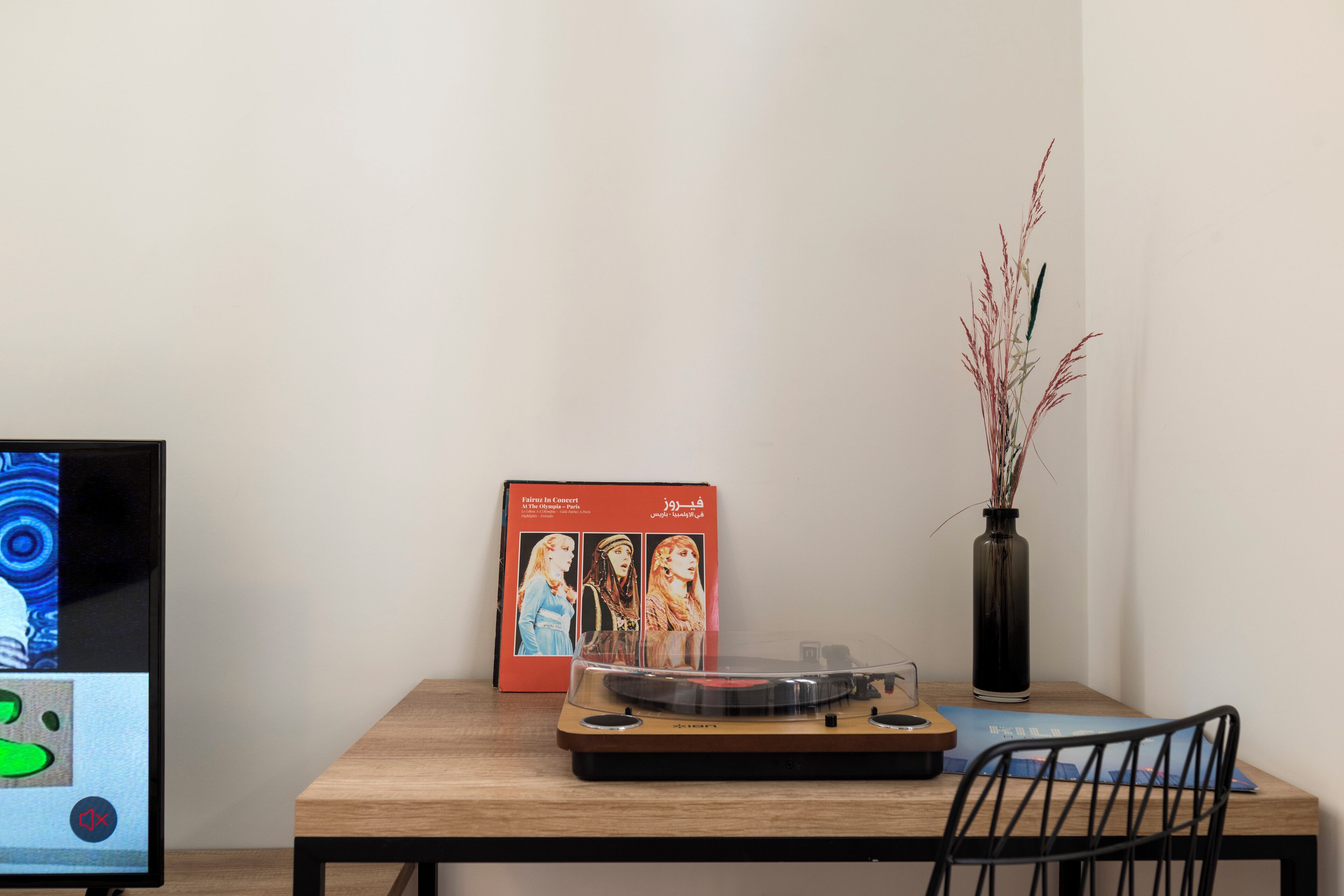 Una mesa de madera con un tocadiscos, un cartel enmarcado y un jarrón con plantas.