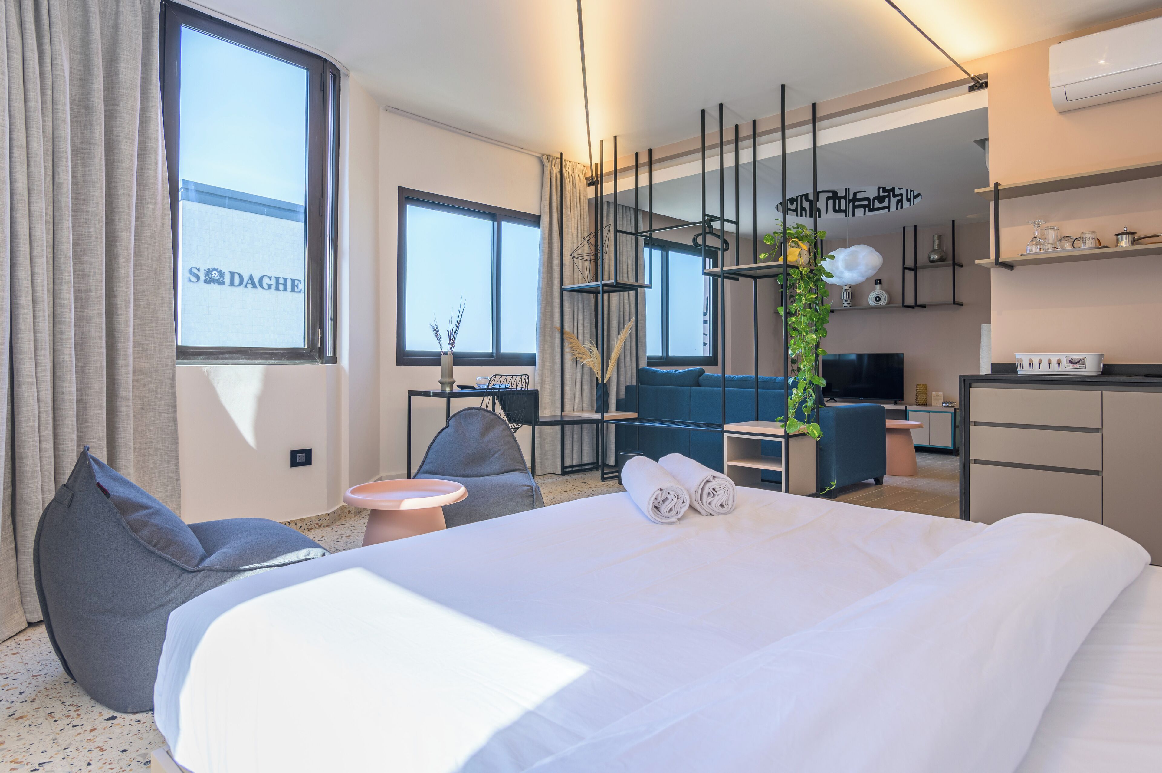 Ett modernt hotellrum med en stor säng, ett skrivbord, en stol och en soffa. Det finns ett fönster med gardiner, en växt och en tv.