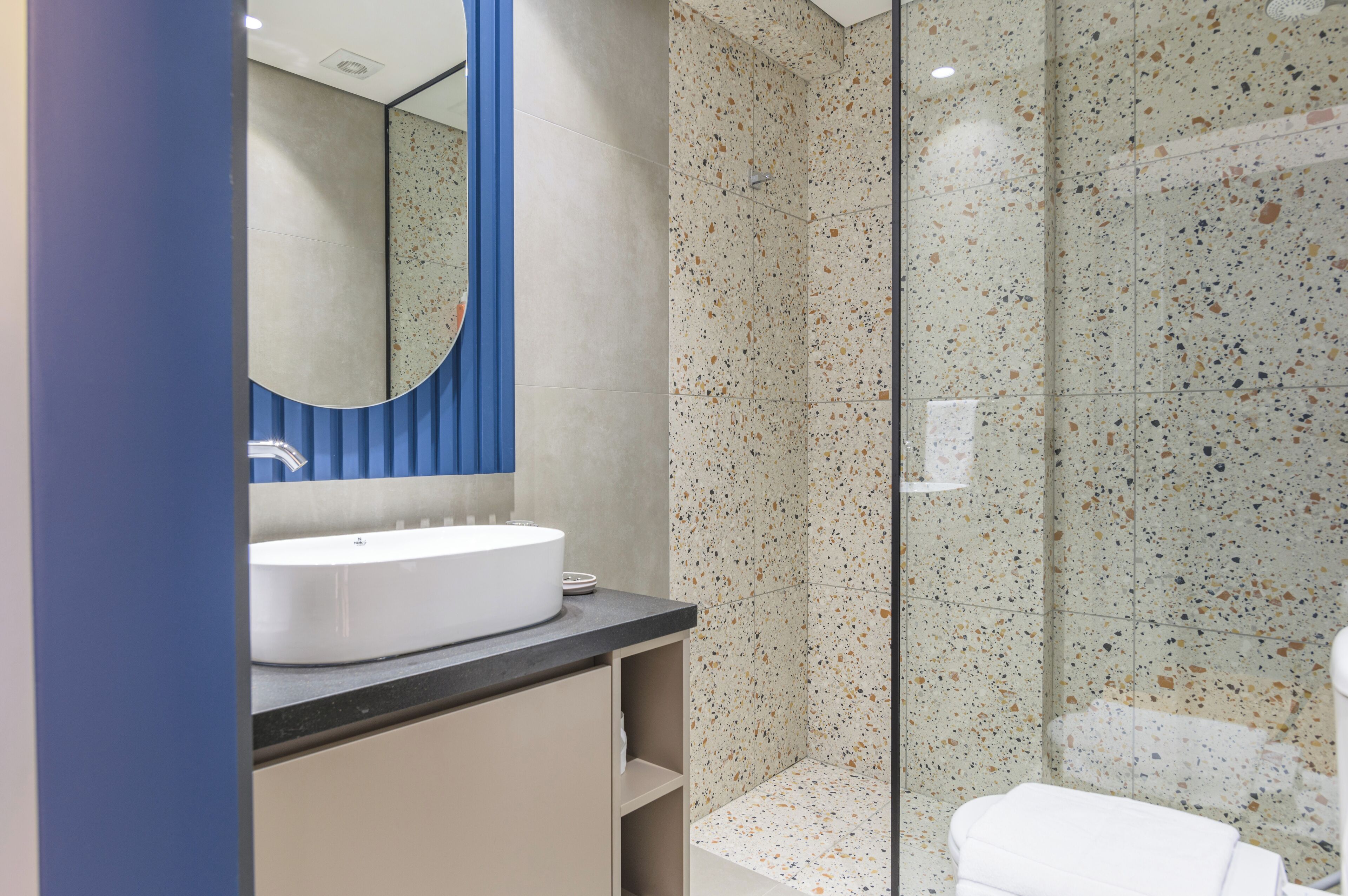 A modern bathroom with a white sink, a mirror with a blue frame, and a shower with speckled tiles.