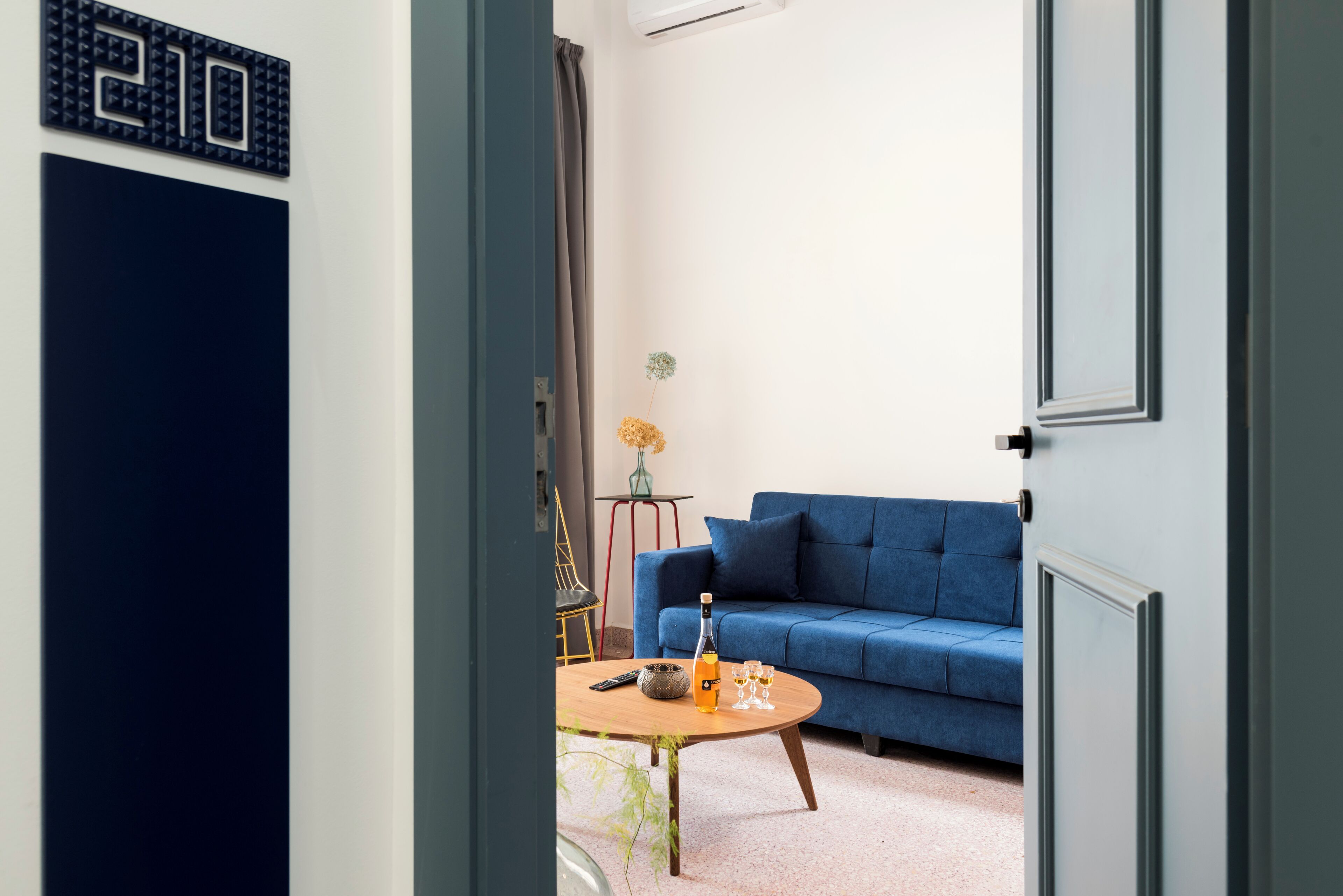 Una sala de estar moderna con un sofá azul, una mesa de centro con una botella y vasos, y una puerta con el símbolo de número.