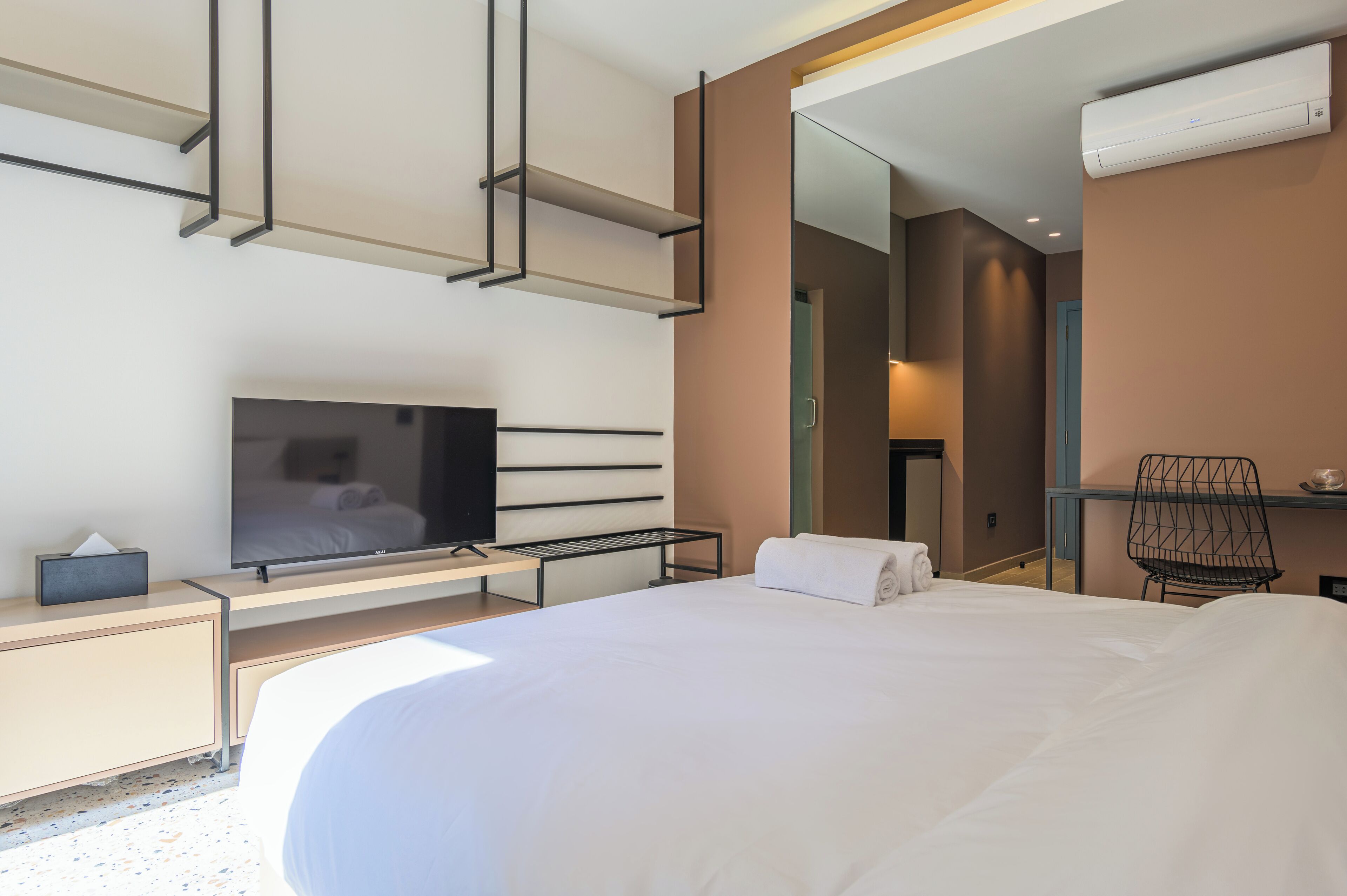 A modern hotel room with a large bed, a flat-screen TV, a desk with a chair, and a mirror.