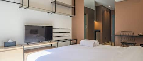 A modern hotel room with a large bed, a flat-screen TV, a desk with a chair, and a mirror.