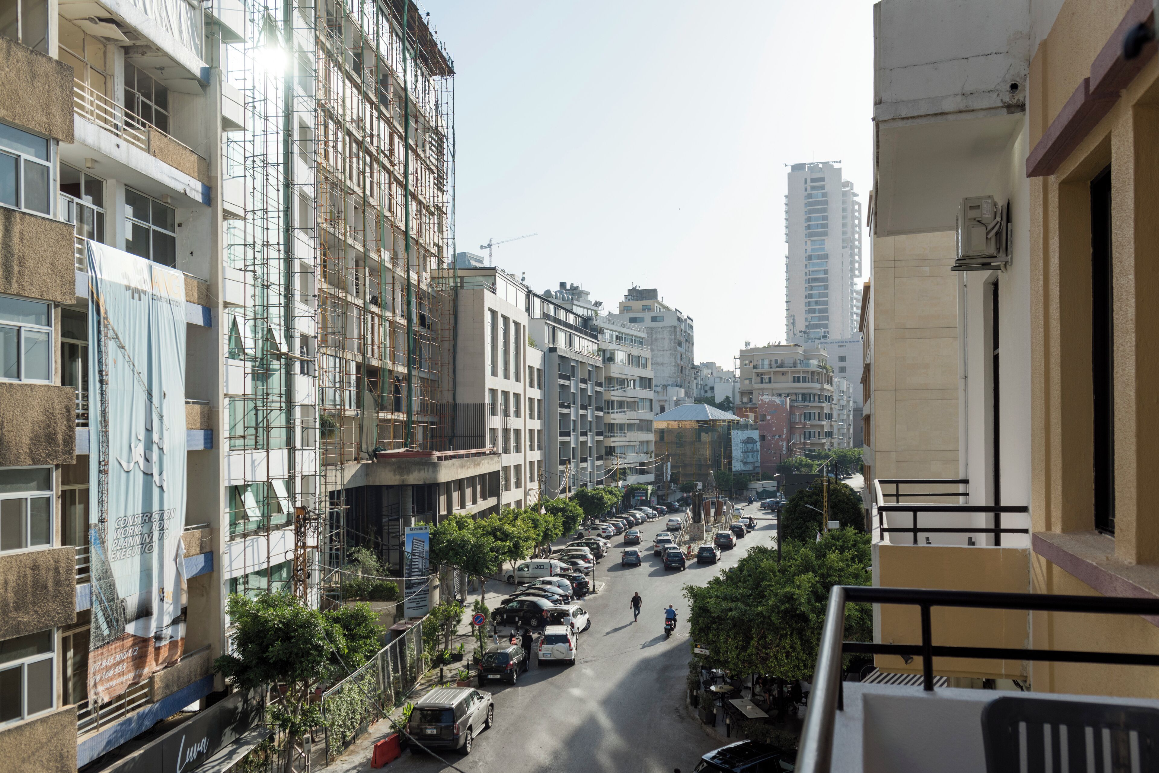 Une vue de rue avec des immeubles à plusieurs étages, des voitures garées et un cycliste.