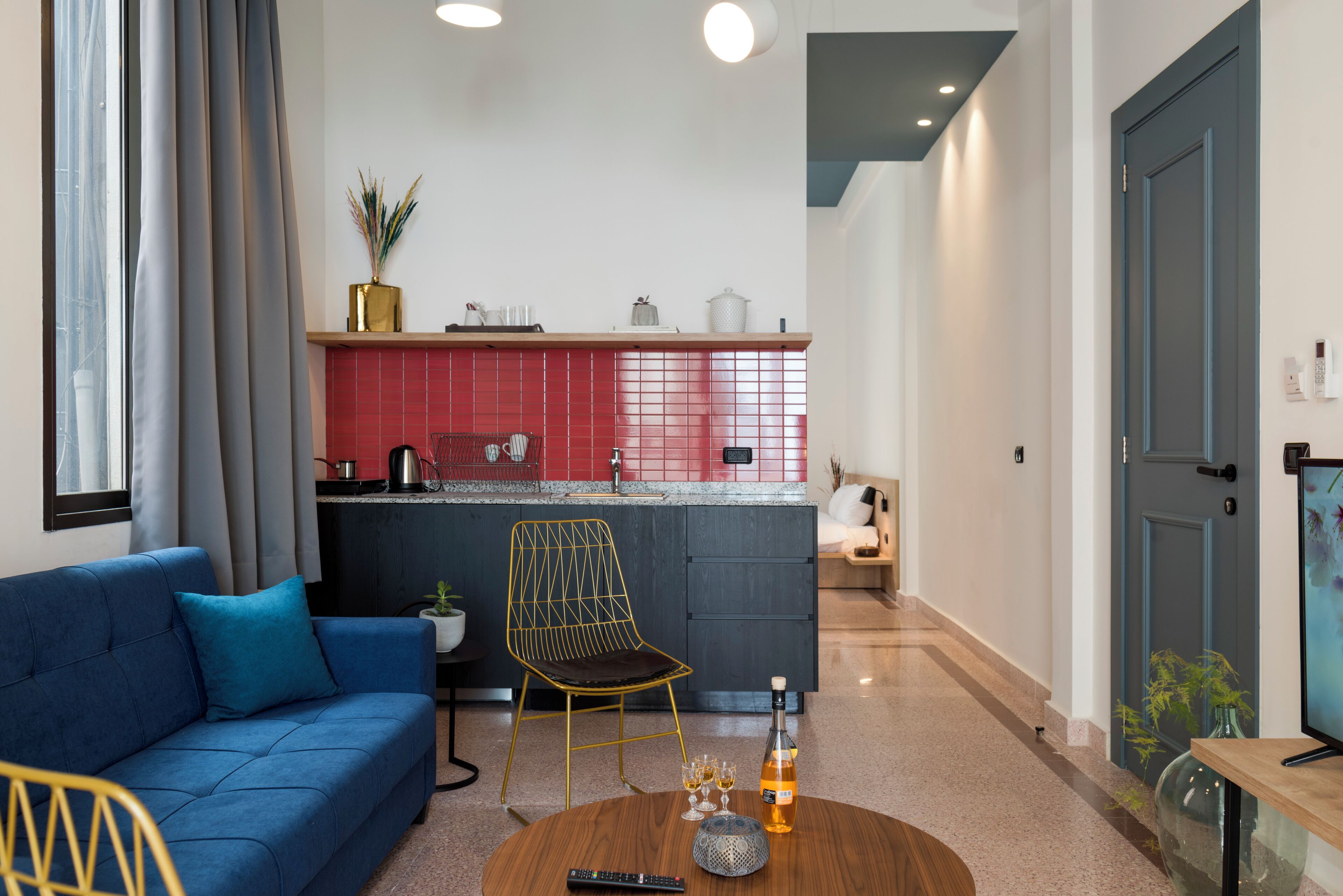 Una sala de estar moderna con un sofá azul, una mesa de centro redonda con un control remoto, una botella y vasos.
