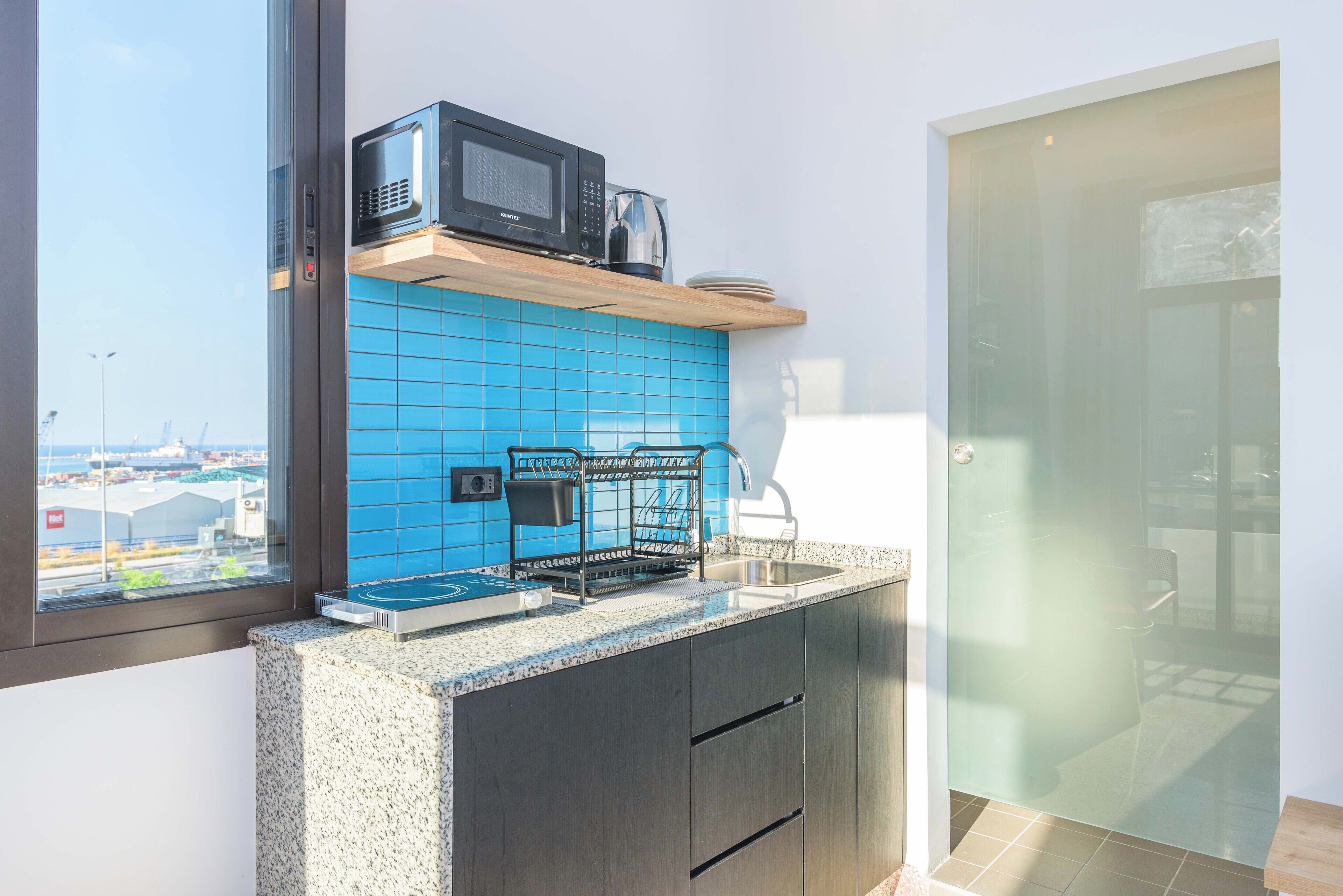 Uma cozinha moderna com painel de azulejos azuis, micro-ondas, máquina de café e pia.