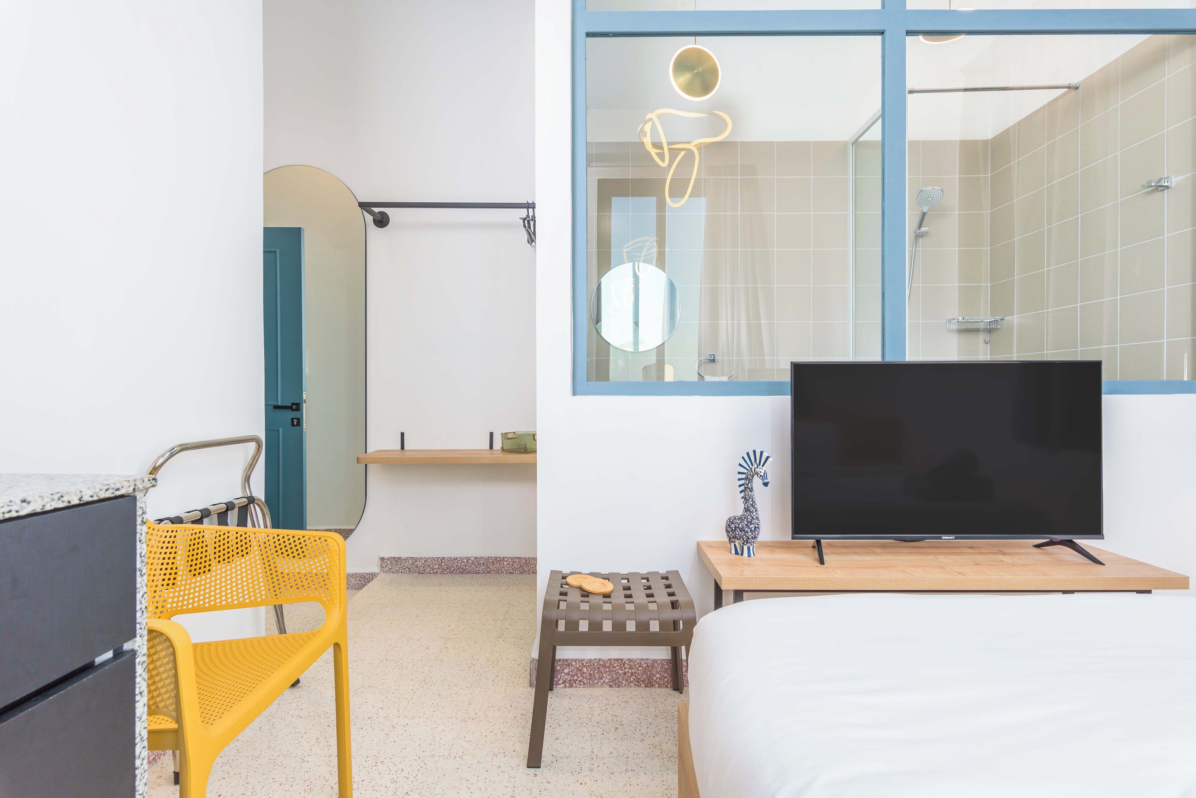 Habitación de hotel con cama, televisión, mesita, silla, zona de ducha y ventana con vistas al exterior.