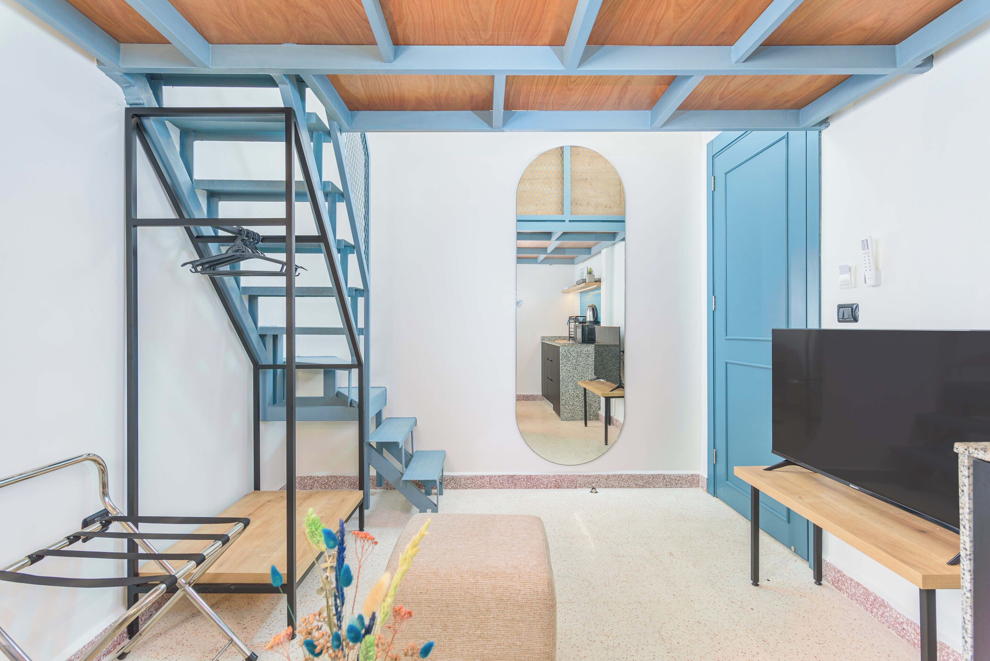 A modern interior with a staircase, a flat-screen TV, and a mirror reflecting a kitchen area.