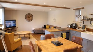 A modern living room with a TV, sofa, dining table, and kitchen area. - Cowshed near Abergavenny in the Black Mountains (Abergavenny)