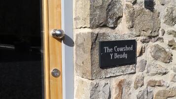 Un muro de piedra con un letrero que dice "The Cowshed Y Bedyu" y una puerta de madera con un picaporte plateado.