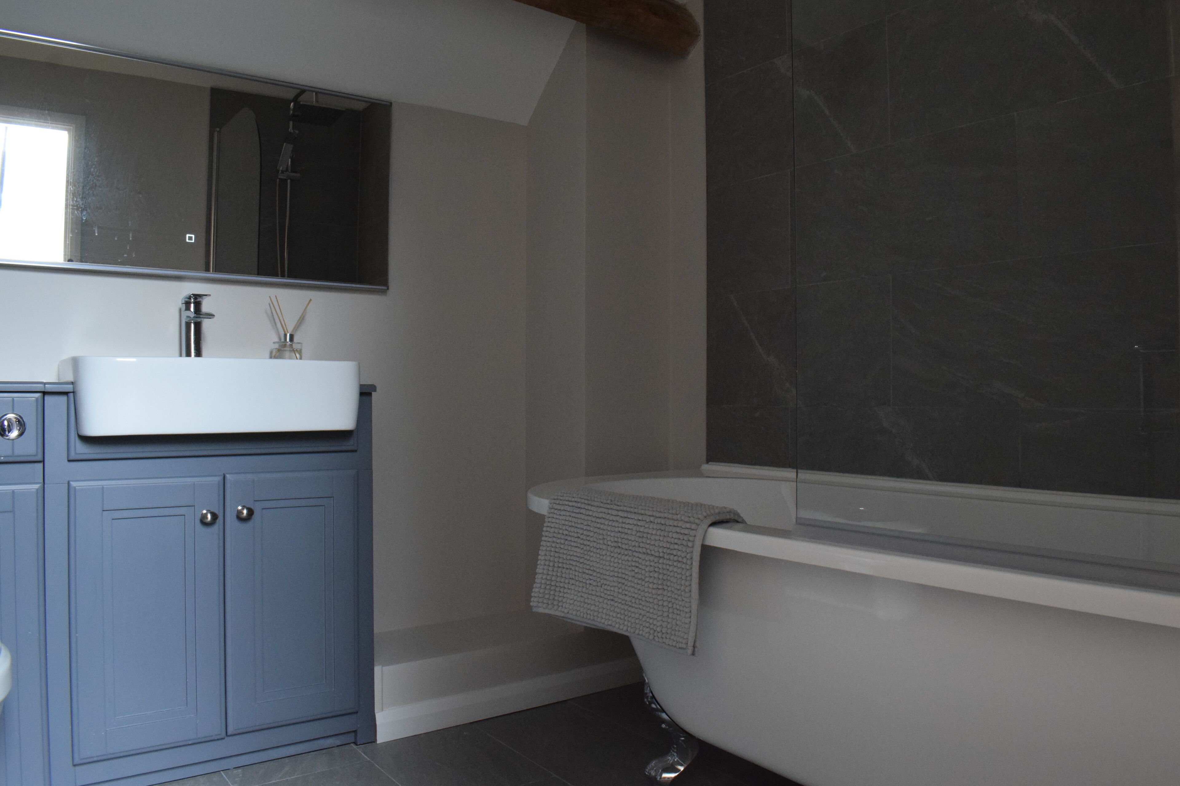 Un bagno moderno con una vasca da bagno indipendente, uno specchio grande e un mobile lavabo blu.