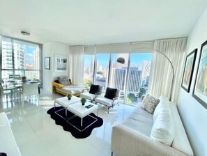 Enjoy a panoramic city view from the large window in this stylish living room, featuring a sofa, coffee table, and dining area.