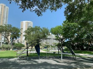 Children can play on the swings and climbing frame in this shaded park surrounded by trees and grass.