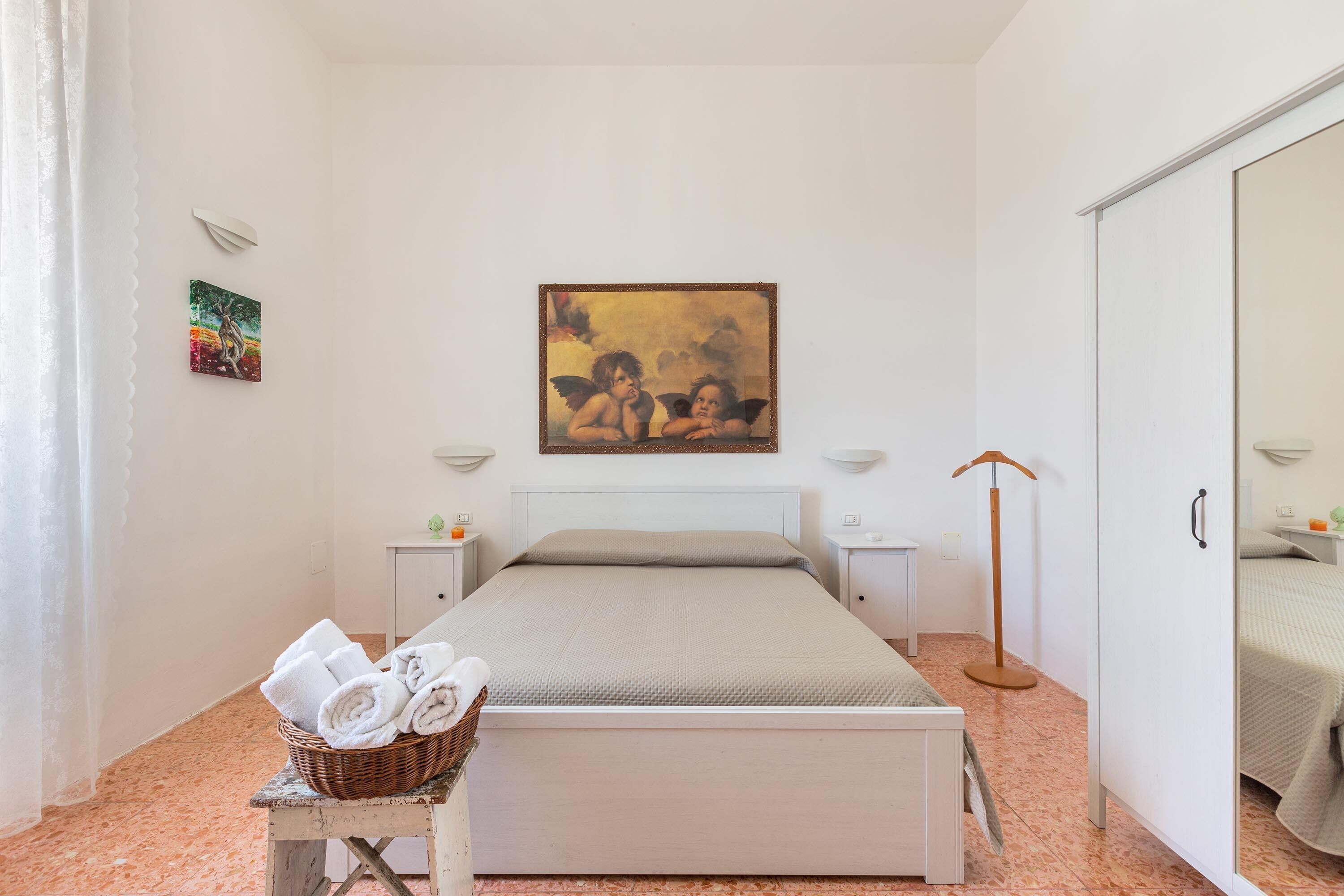 Une chambre à coucher bien rangée, avec un lit, une table de chevet, une lampe et un tableau accroché au mur.
