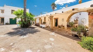 Un cortile con una palma, posti a sedere all'aperto e un edificio con un arco.