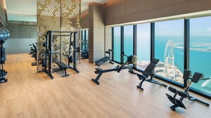 A gym with various exercise equipment, large windows with a view of a coastal cityscape and a prominent bridge. - Maison Privee - Lavish Apt w/ Stellar Ocean Views in Address JBR (Dubai)