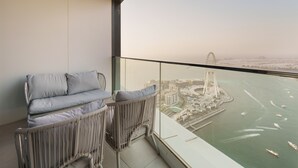 A balcony with a sofa and a chair, overlooking a body of water with a bridge and buildings. - Maison Privee - Lavish Apt w/ Stellar Ocean Views in Address JBR (Dubai)