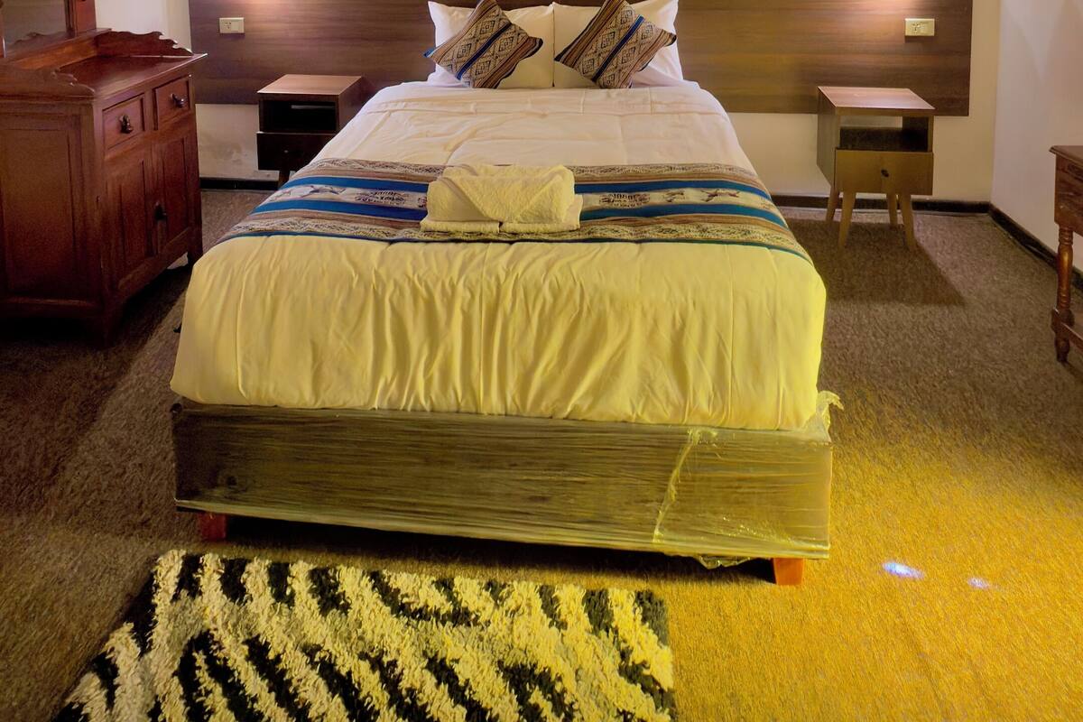 Een netjes ingerichte slaapkamer met een groot bed, nachtkastjes, een houten hoofdbord en een hanglamp.