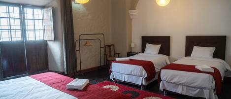 A hotel room with two beds, a red and white patterned rug, and hanging light fixtures.