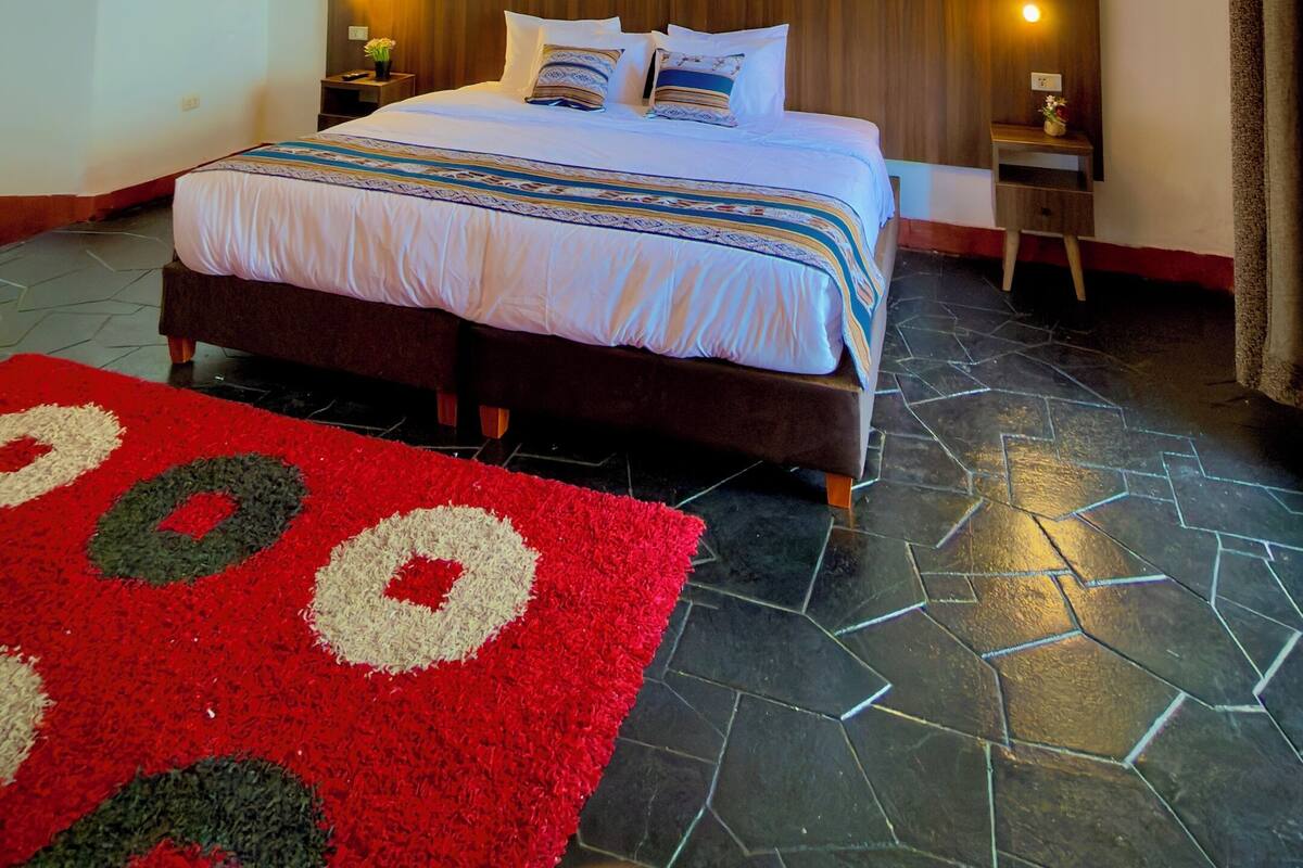 Een slaapkamer met een bed, twee nachtkastjes, een schilderij en een tapijt met een rood-wit patroon.