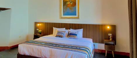 A bedroom with a bed, two bedside tables, a painting, and a red and white patterned rug.