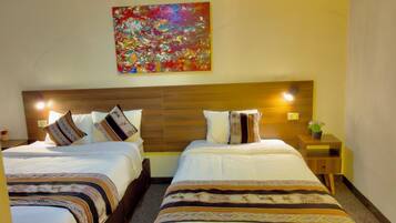 Quarto de hotel com duas camas, cabeceira de madeira, pintura abstrata colorida e uma pequena mesa com uma planta.