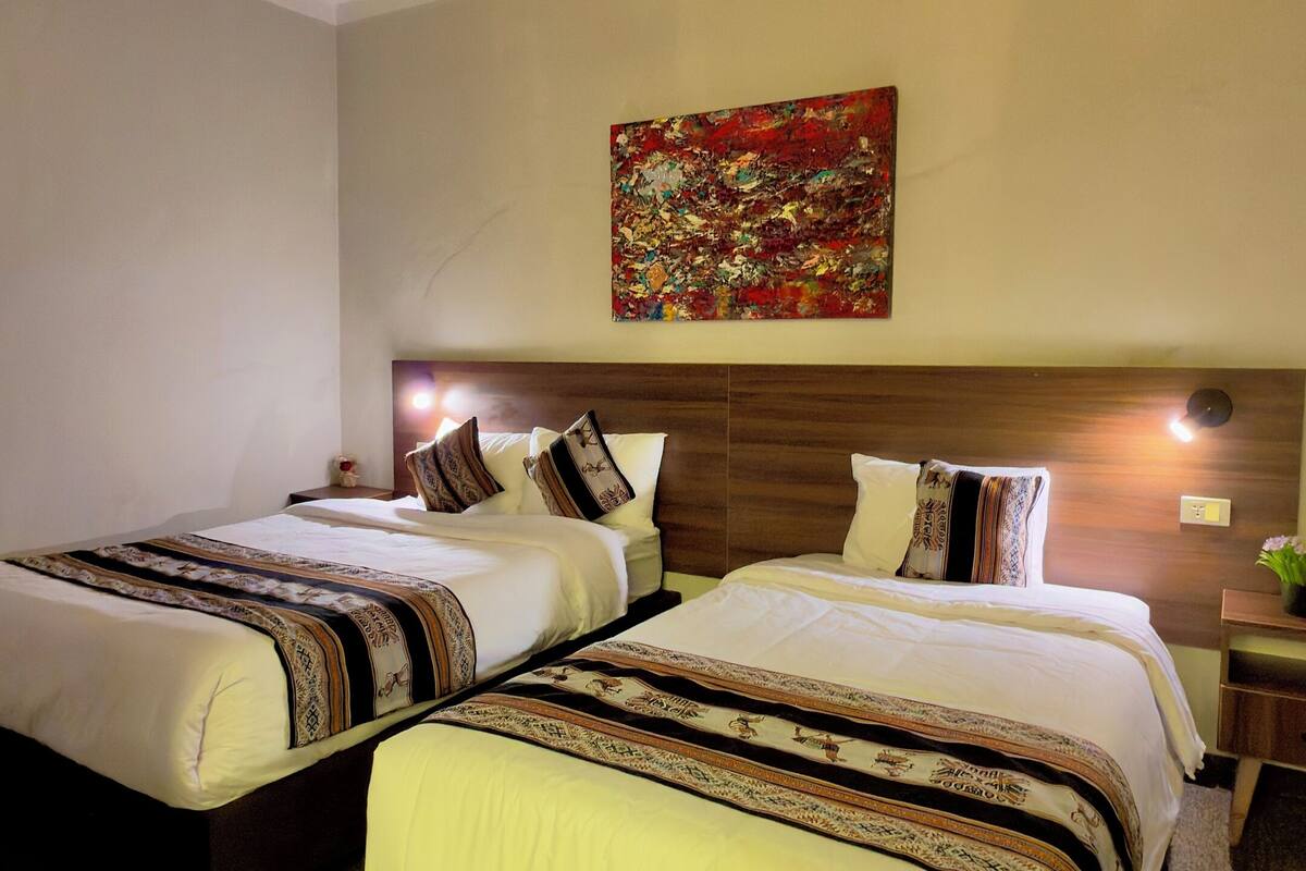 Een hotelkamer met twee bedden, een houten hoofdbord, een abstract schilderij in het rood en een plafondlamp.