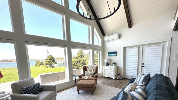 A spacious living room with large windows, a fireplace, and a view of the outdoors. - Water View Cottage With Access To River & Minutes To Sandy North Shore Beaches (Kensington)