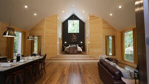 Interior moderno de una cabaña de madera con cama central, comedor y zona de estar.