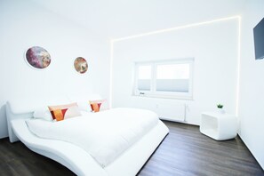 A modern bedroom with a large bed, a bedside table, a window, and two wall art pieces.