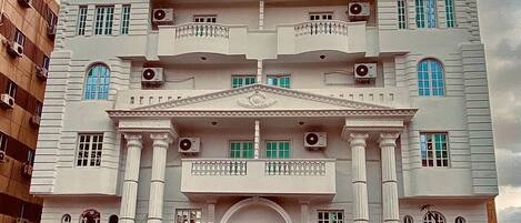 A multi-story building with a central entrance, balconies, and air conditioning units.