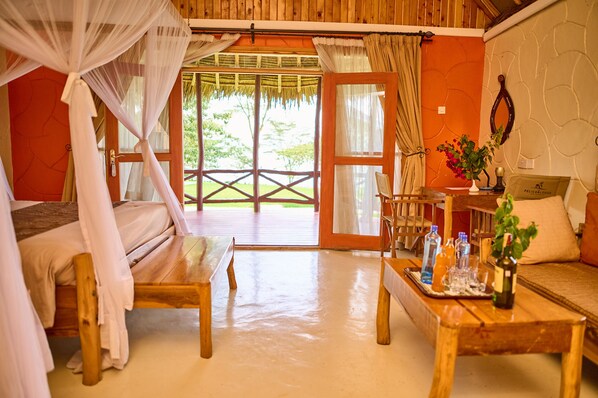 A room with a bed, a wooden table with drinks, a sofa, and a view of greenery outside.