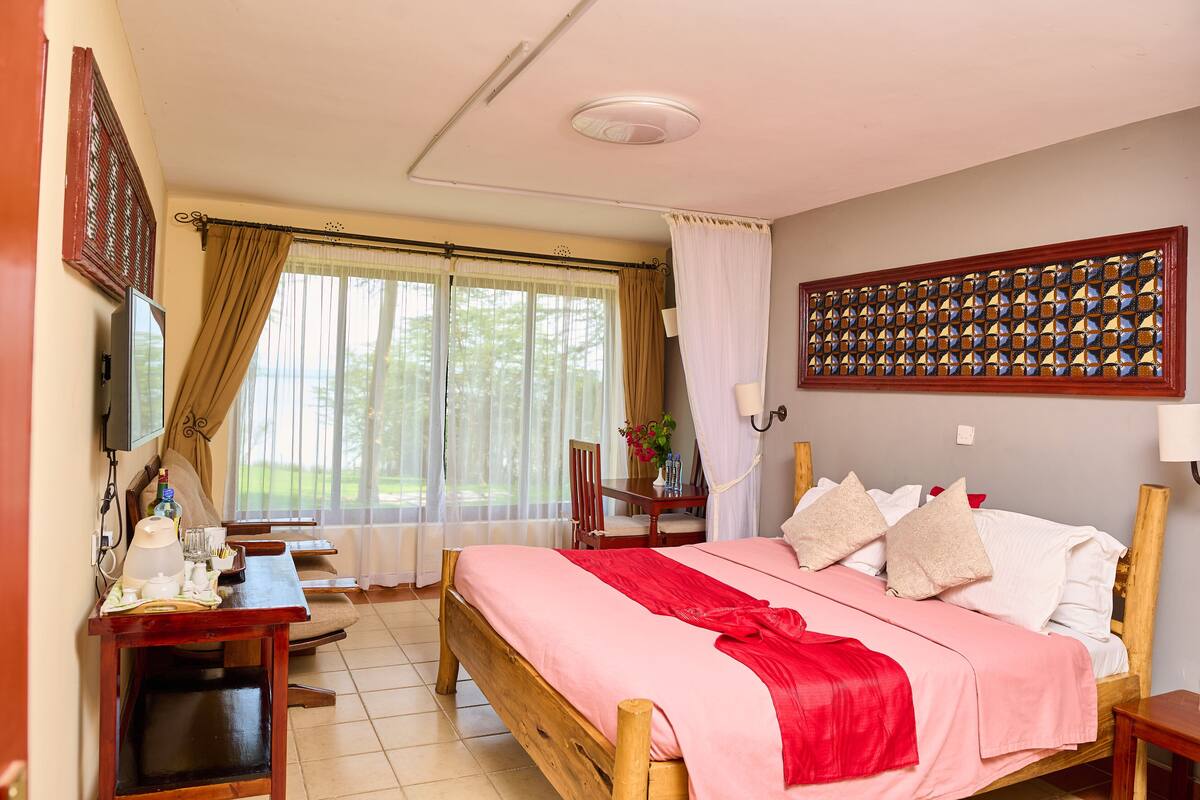 Quarto de hotel com cama, escrivaninha, cadeira, televisão e janela com cortinas.