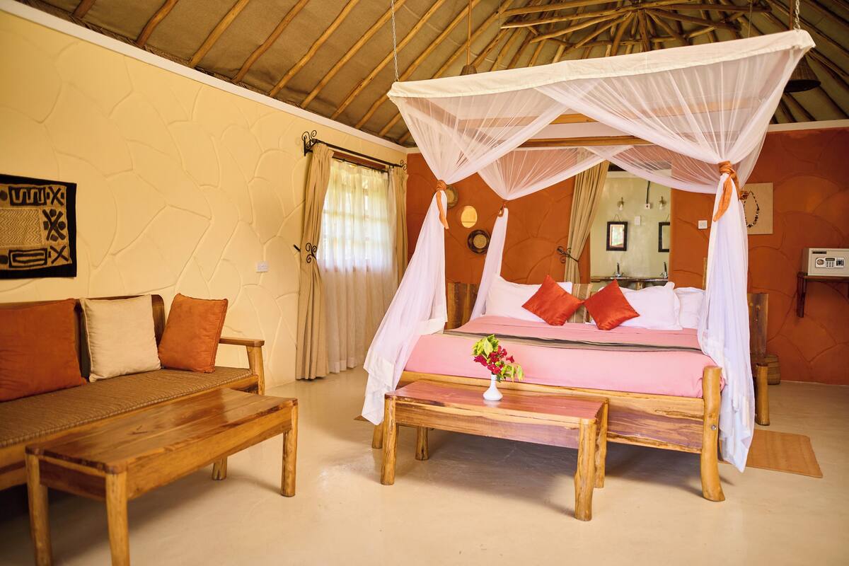 Quarto com cama sob dossel, sofá, mesa de madeira e parede com padrão decorativo.