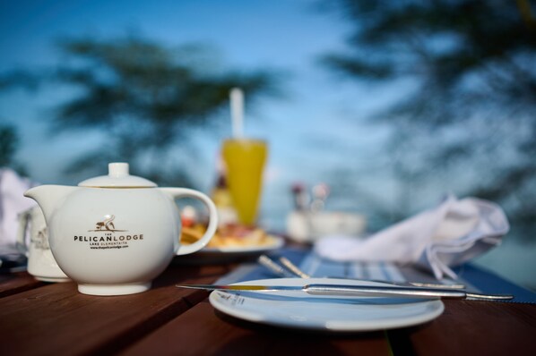 A table with a teapot, a yellow drink, and a plate with cutlery.