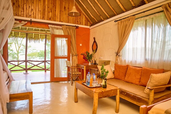 A wooden-floored room with a sofa, a table with bottles, and a chair. - PELICAN LODGE - LAKE ELEMENTAITA (Gilgil)