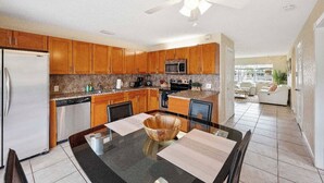 A modern kitchen with wooden cabinets, stainless steel appliances, and a dining area with a glass table. - Waterfront-2BDR/2BTH -4 mins to the Beach+ Kayaks (Pompano Beach)