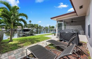 Un espace extérieur abrité comprenant un barbecue, des chaises longues et une vue sur une marina remplie de bateaux.