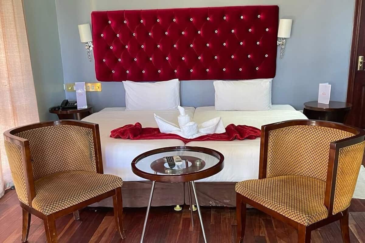 A hotel room with a large bed, two chairs, a small round table, and a red throw blanket.